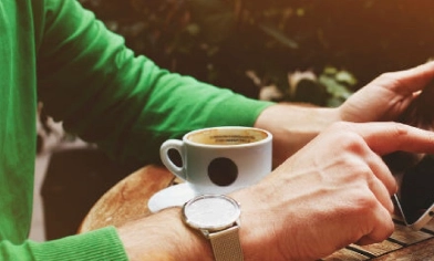 a person in a green jumper browsing a tablet and having coffee