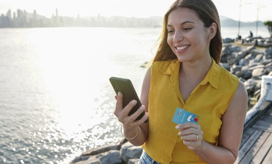 a person on a dock smiling at a smartphone while holding a credit card