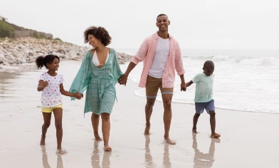 Young family of four walking along a sandy beach with waves to their left