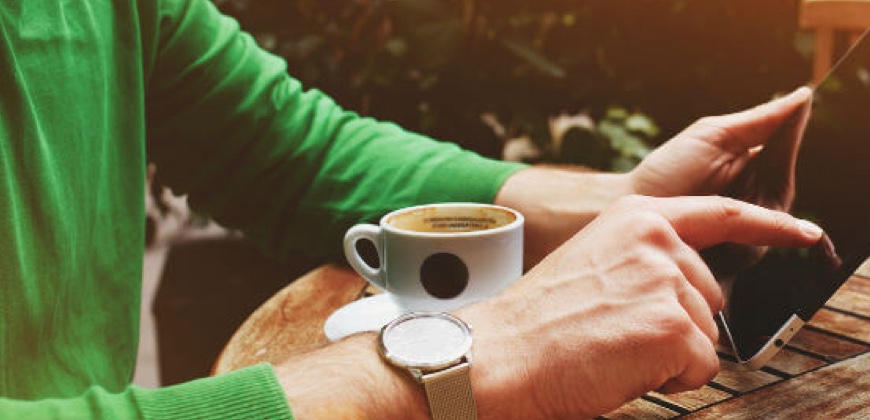 a person in a green jumper browsing a tablet and having coffee