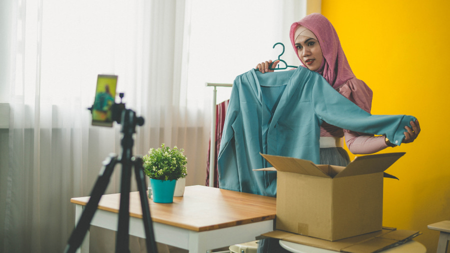 Woman holding up an item of clothing facing toward a mobile phone taking a timed photo of her