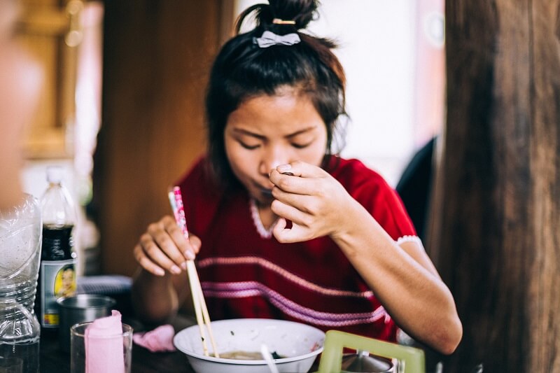 Woman sitting in a restaurant holding chopsticks eating soup