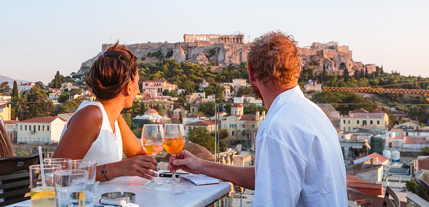 Couple dining outdoors in Athens holding wine glasses looking out to ruins