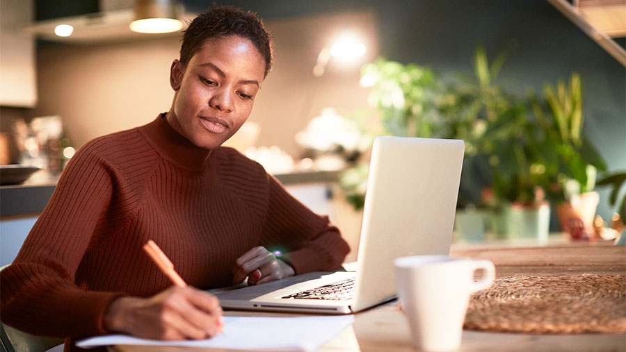 a person sitting at a laptop writing on a piece of paper