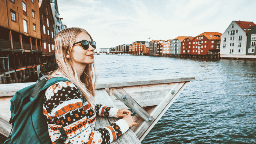 A female tourist on a riverbank in Norway, with the river and buildings in the background