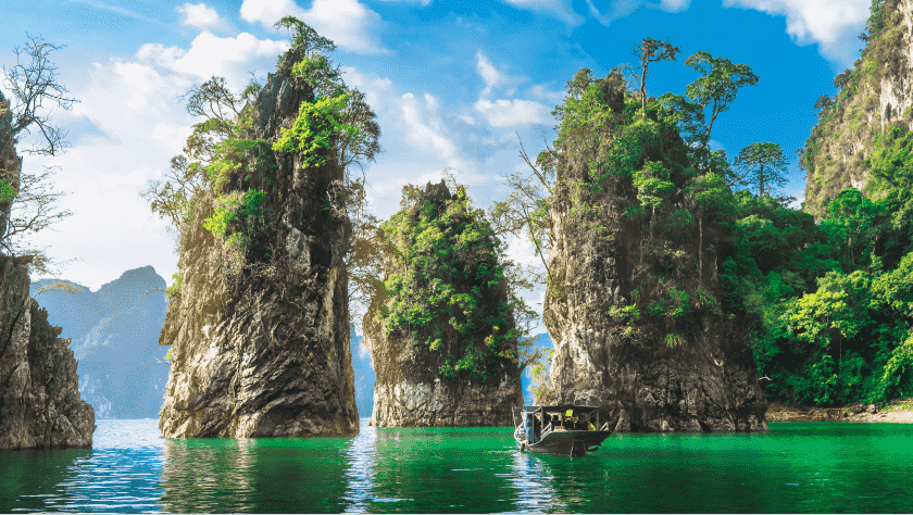 A tourist boat in the Vietnamese seas, surrounded by exotic rocks, trees, mountains, and greenery