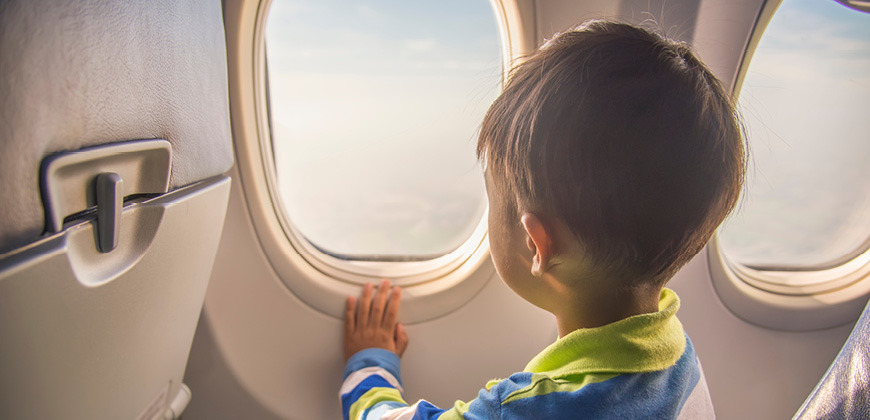 Young boy sitting in airplane looking out of airplane window